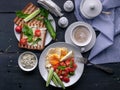 Tasty and healthy breakfast. Fried eggs, vegetable salad, toasts with cream cheese and arugula and cappuccino on a dark background Royalty Free Stock Photo