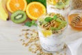 Tasty and healthy breakfast or snack: yogurt, granola and kiwi, orange, banana slices, honey, mint leaves on a white wooden backgr Royalty Free Stock Photo