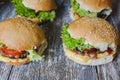 Tasty homemade cheeseburger with mustard, tomatoes and green lettuce. Sesame burgers on wooden background.