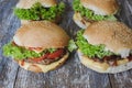 Tasty homemade cheeseburger with mustard, tomatoes and green lettuce. Sesame burgers on wooden background.