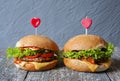 Tasty homemade cheeseburgers with mustard, tomatoes and green lettuce. Sesame burgers with red hearts on wooden background. Food