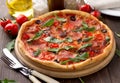 Tasty homemade pizza with ham, tomatoes, cheese, olives and herbs on wooden table. Royalty Free Stock Photo