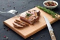 Tasty homemade well-done steak on wooden cutting board with fork and knife on stone background. Royalty Free Stock Photo