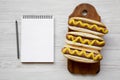 Tasty hot dog with yellow mustard on wooden board and blank notepad on white wooden background, top view. Flat lay, overhead, from Royalty Free Stock Photo