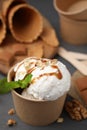 Tasty ice cream with caramel sauce, mint and nuts in paper cup on grey wooden table Royalty Free Stock Photo