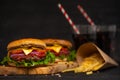 Tasty juicy beef burger, french fries and sweet soda drink on a wooden board on a black background. Hot cheeseburger cooked with