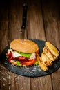 Tasty, juicy hamburger with potato, ketchup and fresh vegetables on stone board with knife. Royalty Free Stock Photo