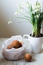 Mini donuts in a paper bag and snowdrops flowers on a white, woode table