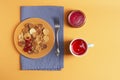 Tasty mini pancakes in an orange plate stand on a blue napkin, next to it is a blue mug with berry drink and a jar of jam