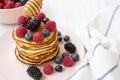 Tasty pancakes with berries and honey on a pink plate, side view.