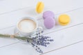 Sweet delicious violet and yellow macarons and cup of latte or americano and branch of fragrant lavender on white wooden