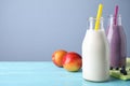 Tasty peach and blueberry milk shakes in bottles on light blue wooden table