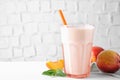 Tasty peach milk shake in glass and fresh fruit on white table