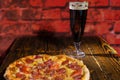 Tasty pepperoni pizza on wooden table near a glass of dark beer Royalty Free Stock Photo