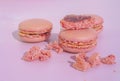 Tasty pink raspberry macarons on light violet background. French homemade dessert with small broken pieces