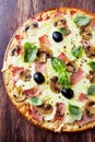 Tasty pizza with ham, champignon mushrooms, mozzarella cheese, black olives and fresh basil on wooden background. Royalty Free Stock Photo