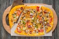 Tasty pizza with mushrooms, chicken, pepperoni, olives, corn cut into pieces on a wooden tray. Royalty Free Stock Photo