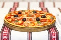 Tasty pizza with vegetables, basil, olives, tomatoes, green pepper on cutting board, table cloth traditional colorful Royalty Free Stock Photo