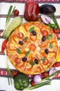 Tasty pizza with vegetables, basil, olives, tomatoes, green pepper on cutting board, table cloth traditional colorful Royalty Free Stock Photo