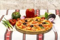 Tasty pizza with vegetables, basil, olives, tomatoes, green pepper on cutting board, table cloth traditional colorful Royalty Free Stock Photo