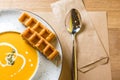 Tasty pumpkin cream soup with Belgian waffles slices on white plate and wooden table. Cafe, restaurant or home cooking Royalty Free Stock Photo