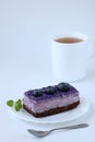 Tasty purple blueberry mousse cake with blueberry on white plate with teaspoon and cup of tea white background, vertical Royalty Free Stock Photo