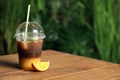 Tasty refreshing drink with coffee and orange juice in plastic cup on wooden table against blurred background, space for text Royalty Free Stock Photo