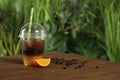 Tasty refreshing drink with coffee and orange juice in plastic cup on wooden table against background, space for text Royalty Free Stock Photo