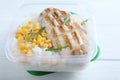 Tasty rice with grilled meat and corn in plastic container on white wooden table, closeup Royalty Free Stock Photo