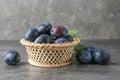 Tasty ripe plums in wicker bowl on grey textured table Royalty Free Stock Photo