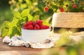 Tasty ripe raspberries in bowl, green leaves and straw hat on wooden table outdoors Royalty Free Stock Photo