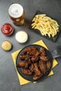 Tasty roasted chicken wings, sauces, french fries and glass of beer on black table, flat lay Royalty Free Stock Photo