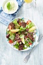 Tasty Salad with Grilled Beef Pieces, Cherry Tomatoes, feta Cheese and Kalamata Olives. Bright wooden background.