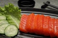 Tasty salmon slices, cucumber and lettuce on plate, closeup. Delicious sashimi dish