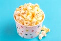 Tasty salty popcorn in paper cup on bright blue background Royalty Free Stock Photo