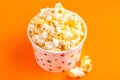 Tasty salty popcorn in paper cup on bright orange backgraund Royalty Free Stock Photo