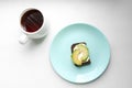 Tasty sandwich with avocado on a turquoise plate and a cup of tea on a white background