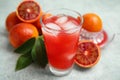 Tasty sicilian orange juice with ice cubes in glass and fruits on light grey table, closeup