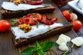 Tasty smorrebrod on a wooden board. Sandwiches with black rye bread, sun-dried tomatoes, salted anchovies, mustard Royalty Free Stock Photo