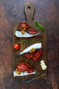 Tasty smorrebrod on a wooden board. Sandwiches with black rye bread, sun-dried tomatoes, salted anchovies, mustard. Top view Royalty Free Stock Photo