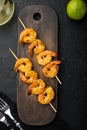 Tasty spiced shrimp skewers  sriracha kebabs with lime, on wooden serving board, on black background, top view flat lay Royalty Free Stock Photo
