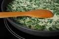 Tasty spinach dip with wooden spoon in frying pan on kitchen stove Royalty Free Stock Photo
