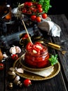 Tasty sun dried tomatoes with garlic, pepper, basil, olive oil in glass jar stands on brass plates on rustic wooden table Royalty Free Stock Photo