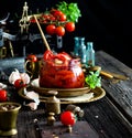 Tasty sun dried tomatoes with garlic, pepper, basil, olive oil in glass jar stands on brass plates on rustic wooden table Royalty Free Stock Photo