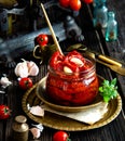 Tasty sun dried tomatoes with garlic, pepper, basil, olive oil in glass jar stands on brass plates on rustic wooden table Royalty Free Stock Photo