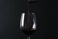 Tasty sweet red wine pouring into tha wineglass against black background