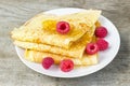 Tasty sweet thin pancakes with fresh raspberries and honey on plate, delicious dessert, closeup, wooden background