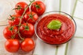 Tasty thick tomato ketchup in a glass bowl and ripe red cherry tomatoes on a twig over white wood kitchen table. Spices,