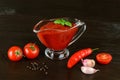 Tasty thick tomato ketchup in a glass gravy boat and red ripe cherry tomatoes, garlic and hot pepper pod on a brown wood table. Royalty Free Stock Photo