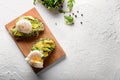 Tasty toasts with avocado and eggs Benedict on wooden board
